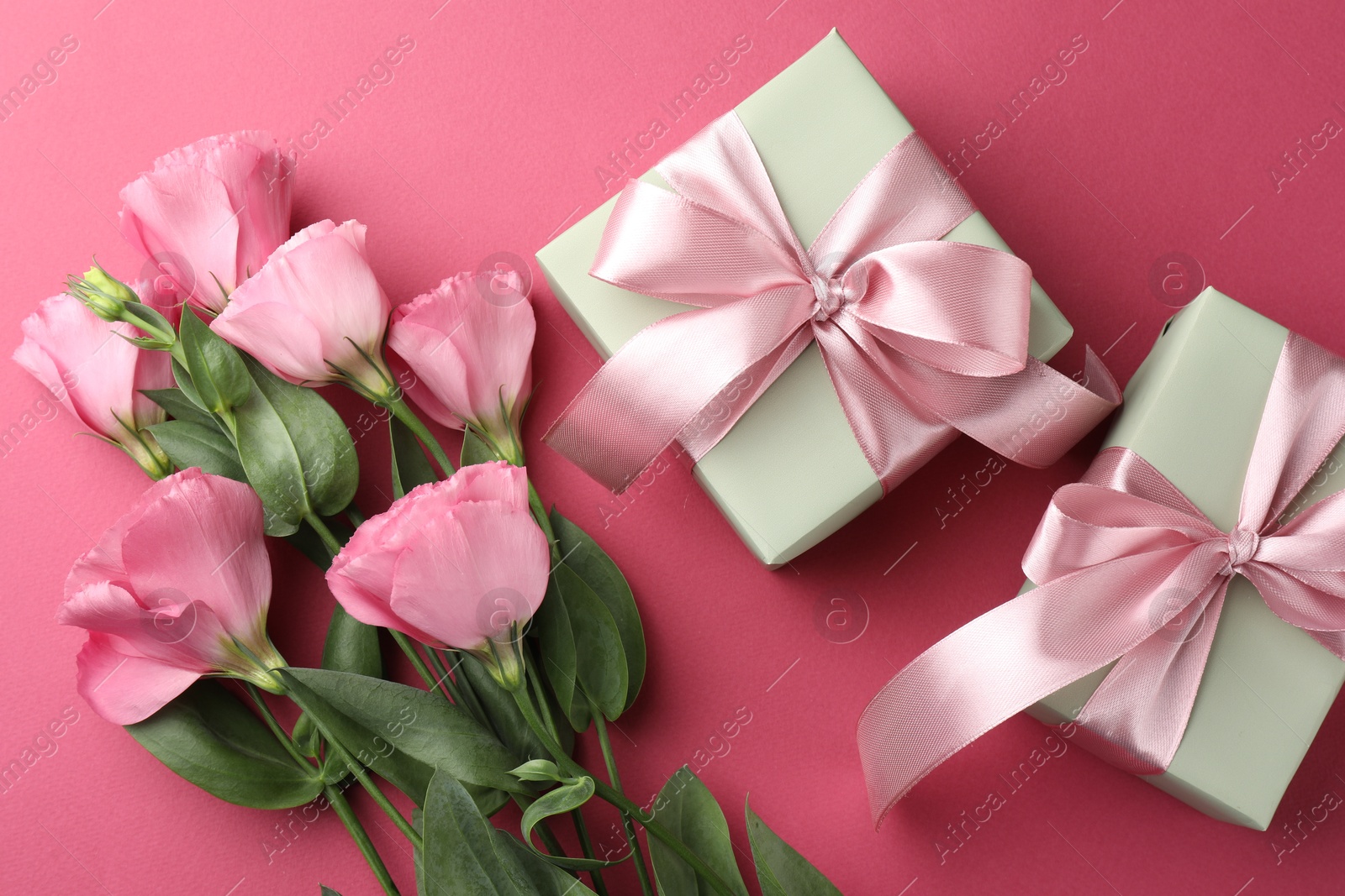 Photo of Beautiful gift boxes with bows and eustoma flowers on pink background, flat lay