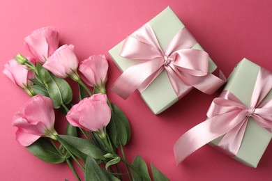 Beautiful gift boxes with bows and eustoma flowers on pink background, flat lay