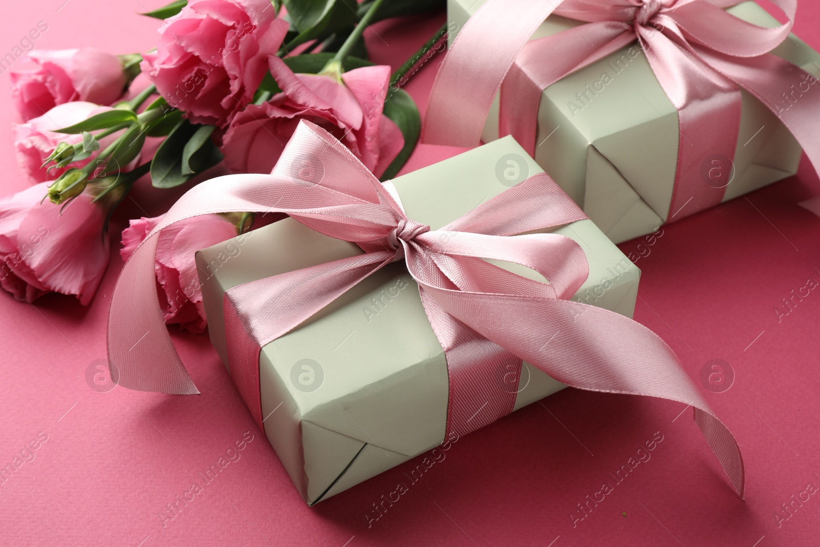 Photo of Beautiful gift boxes with bows and eustoma flowers on pink background, closeup