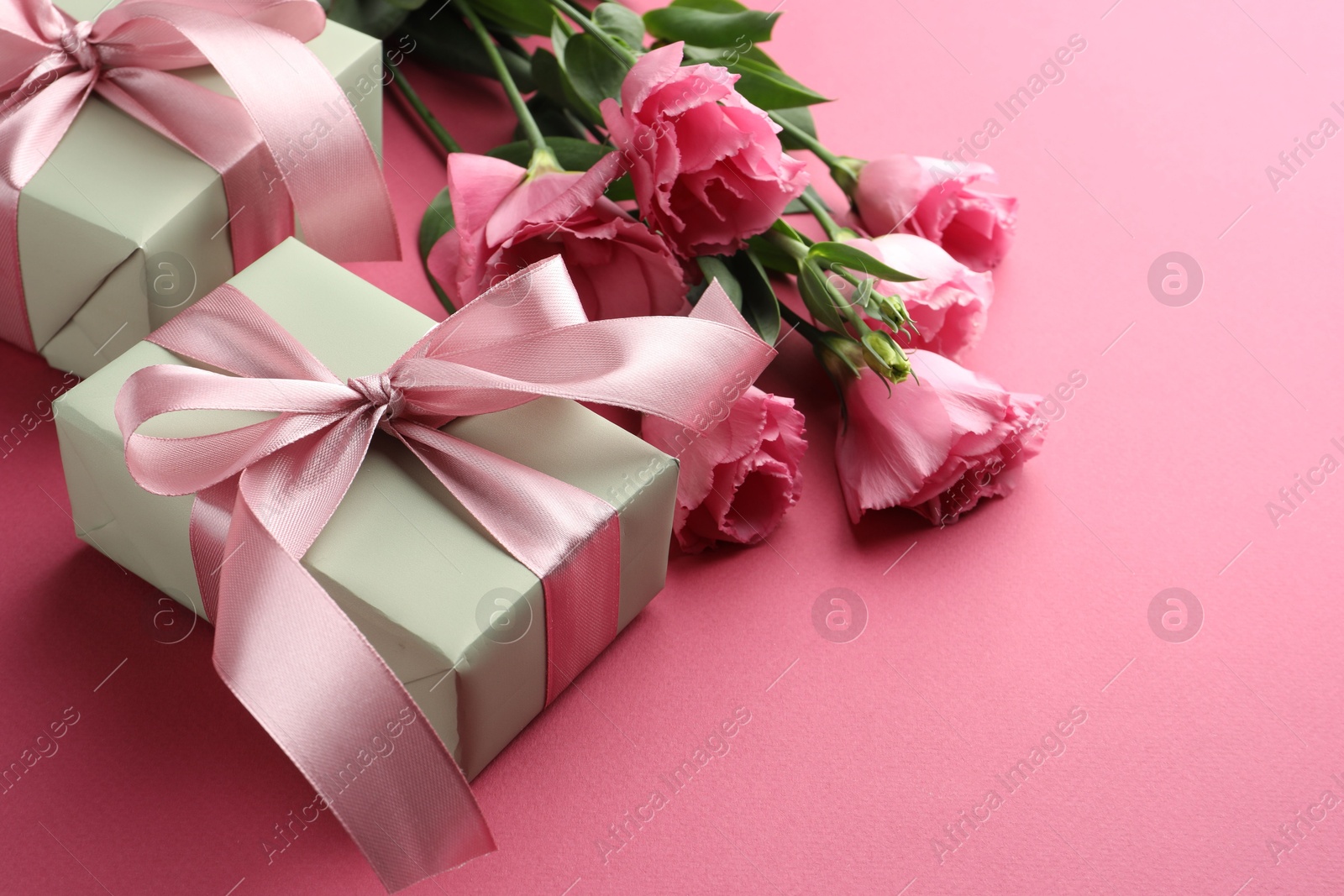 Photo of Beautiful gift boxes with bows and eustoma flowers on pink background