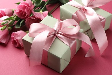 Photo of Beautiful gift boxes with bows and eustoma flowers on pink background, closeup