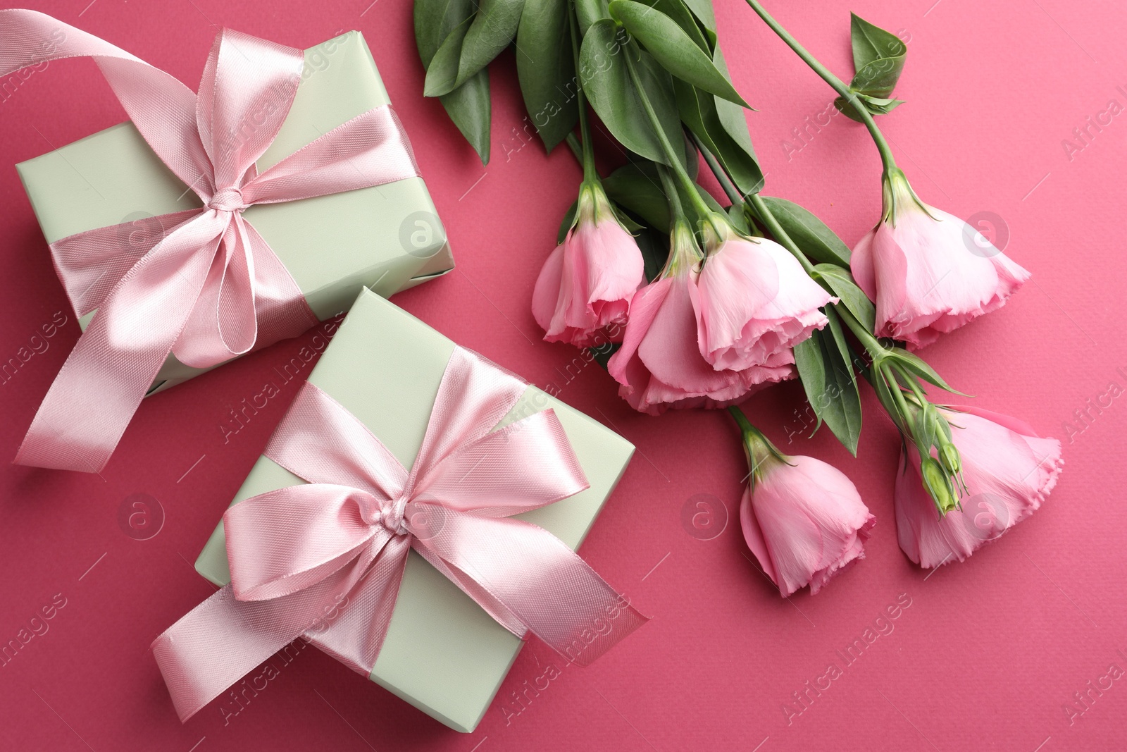 Photo of Beautiful gift boxes with bows and eustoma flowers on pink background, flat lay