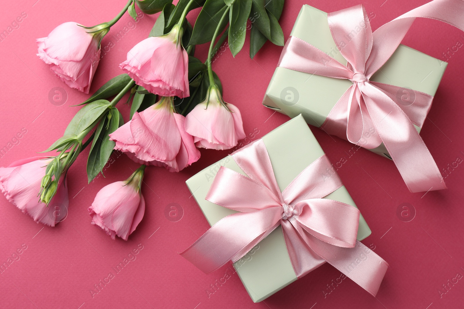 Photo of Beautiful gift boxes with bows and eustoma flowers on pink background, flat lay