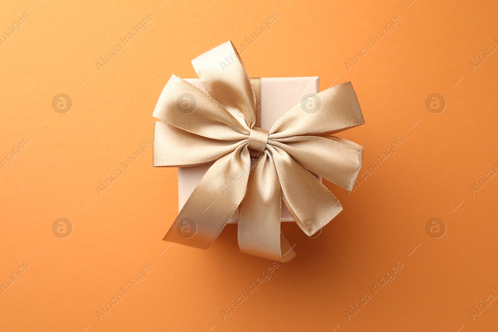 Photo of Beautiful gift box with golden bow on orange background, top view