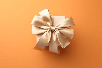 Beautiful gift box with golden bow on orange background, top view