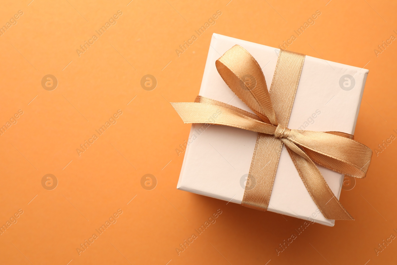 Photo of Beautiful gift box with golden bow on orange background, top view. Space for text