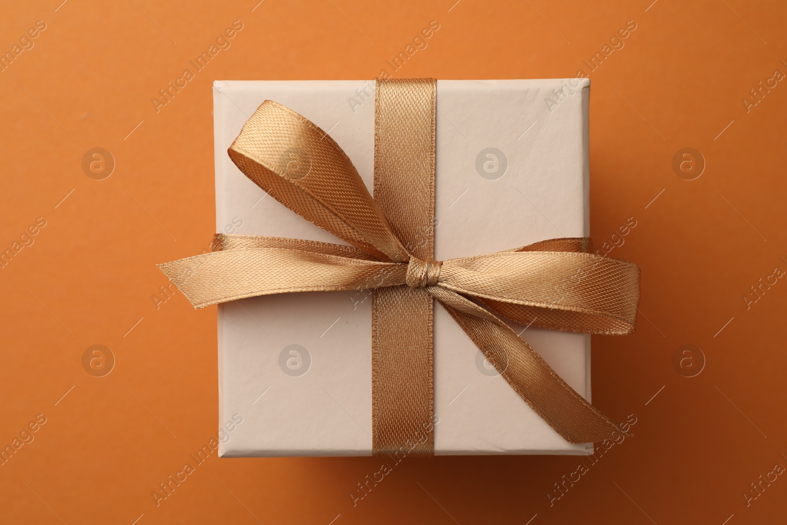 Photo of Beautiful gift box with golden bow on orange background, top view