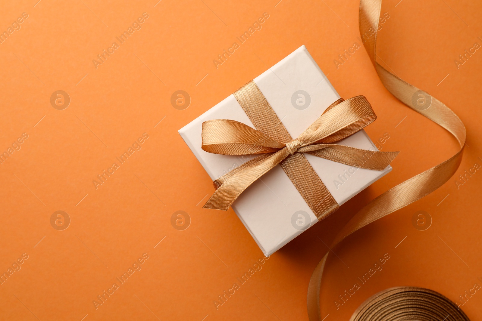 Photo of Beautiful gift box with golden bow and ribbon on orange background, top view. Space for text