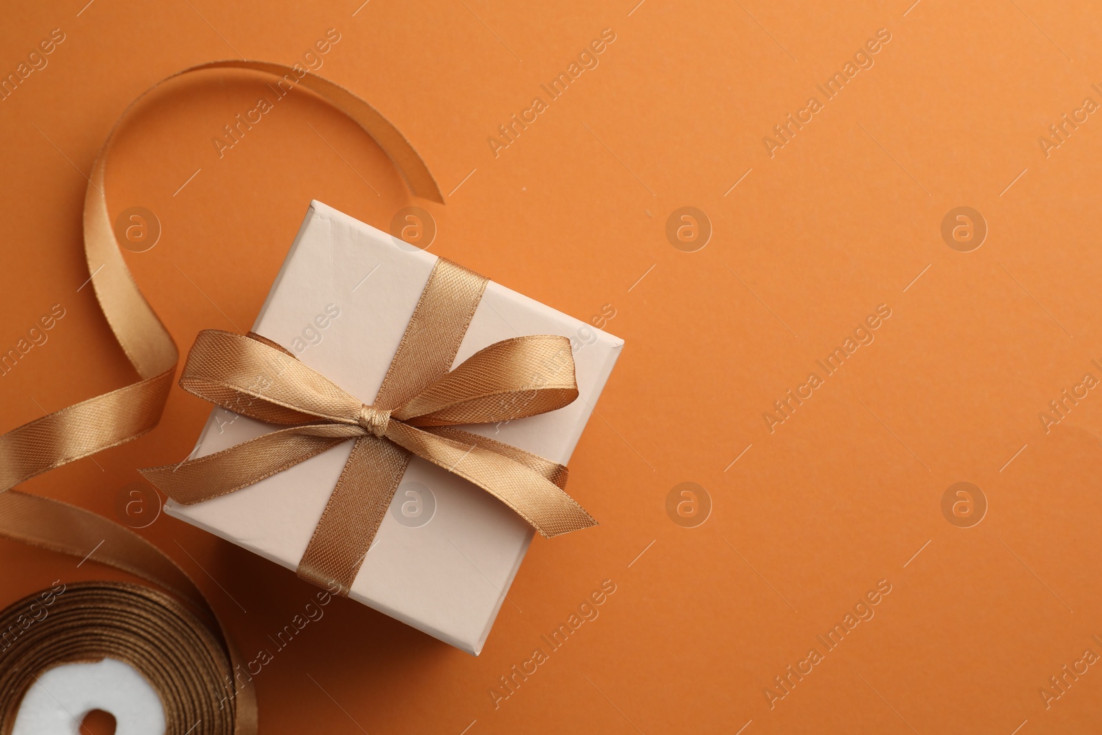 Photo of Beautiful gift box with golden bow and ribbon on orange background, top view. Space for text