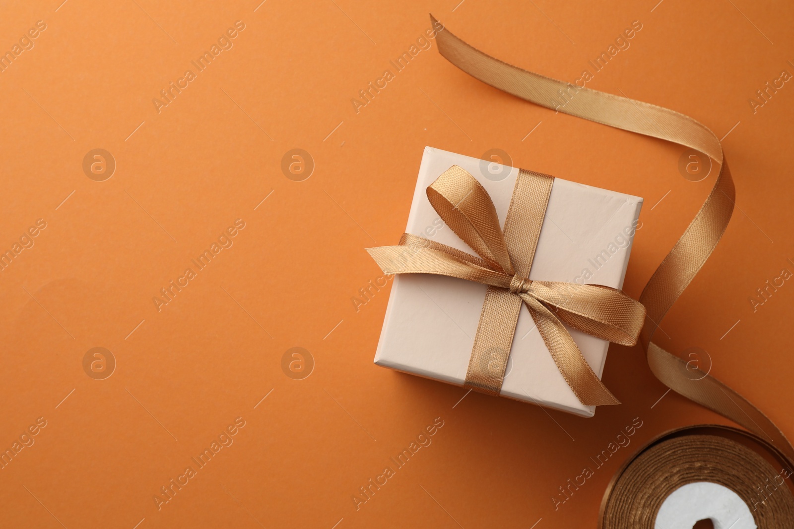 Photo of Beautiful gift box with golden bow and ribbon on orange background, top view. Space for text