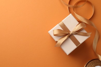 Photo of Beautiful gift box with golden bow and ribbon on orange background, top view. Space for text