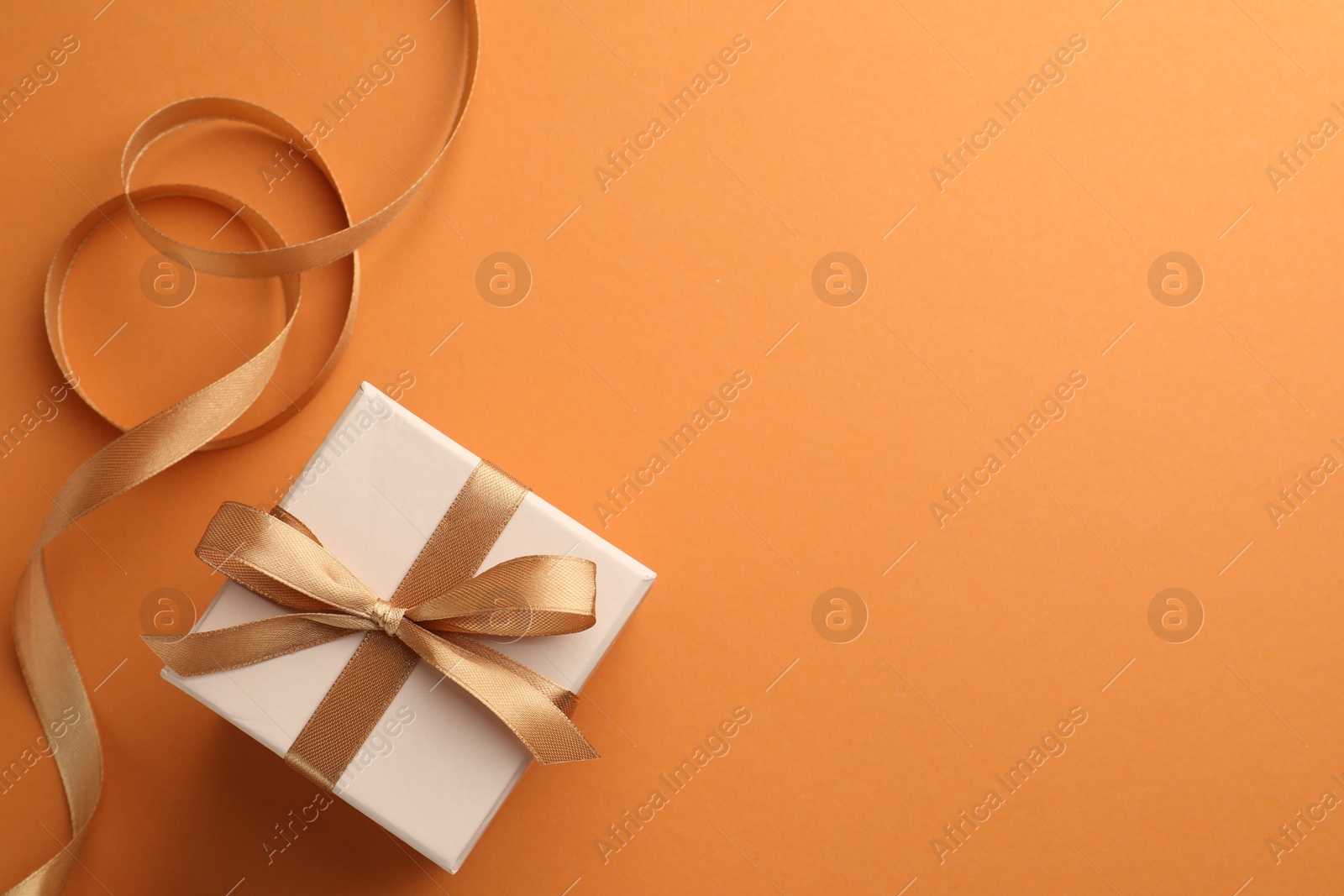 Photo of Beautiful gift box with golden bow and ribbon on orange background, top view. Space for text