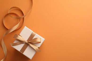 Photo of Beautiful gift box with golden bow and ribbon on orange background, top view. Space for text