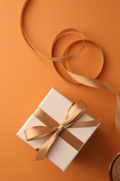 Photo of Beautiful gift box with golden bow and ribbon on orange background, top view