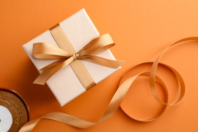 Photo of Beautiful gift box with golden bow and ribbon on orange background, top view