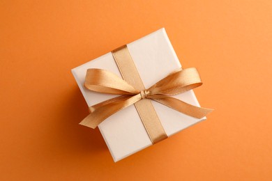 Beautiful gift box with golden bow on orange background, top view