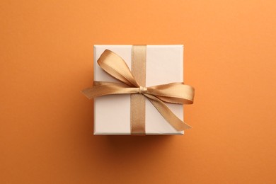 Beautiful gift box with golden bow on orange background, top view