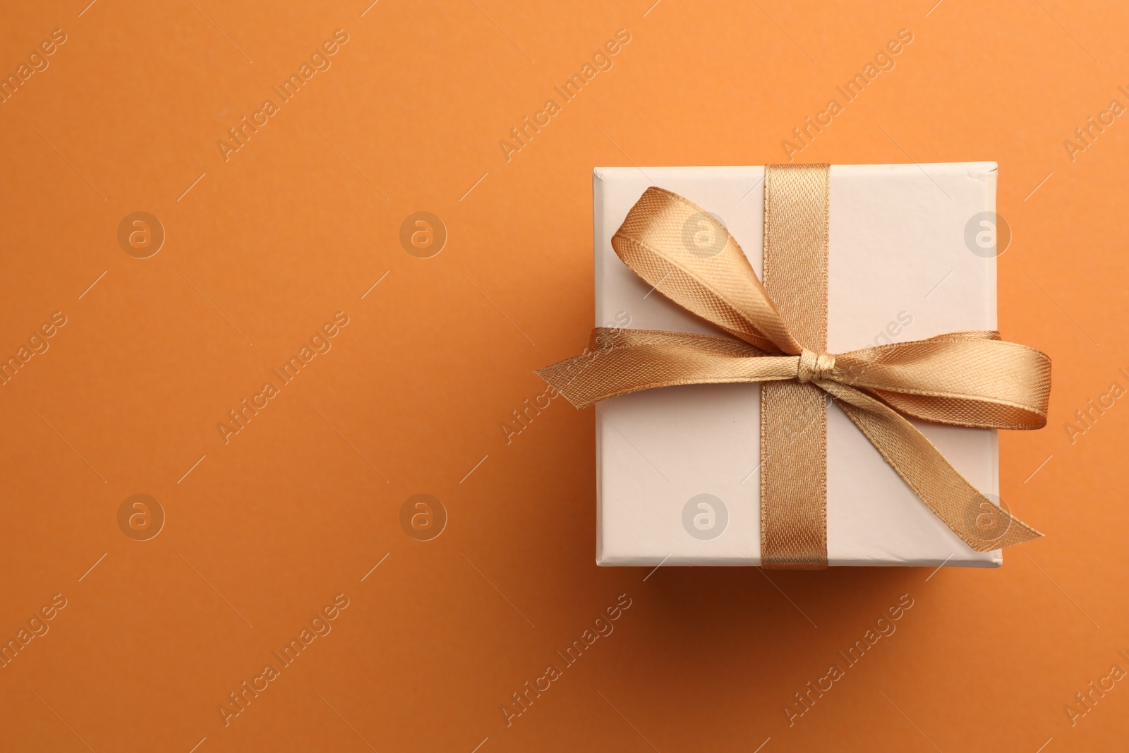 Photo of Beautiful gift box with golden bow on orange background, top view. Space for text