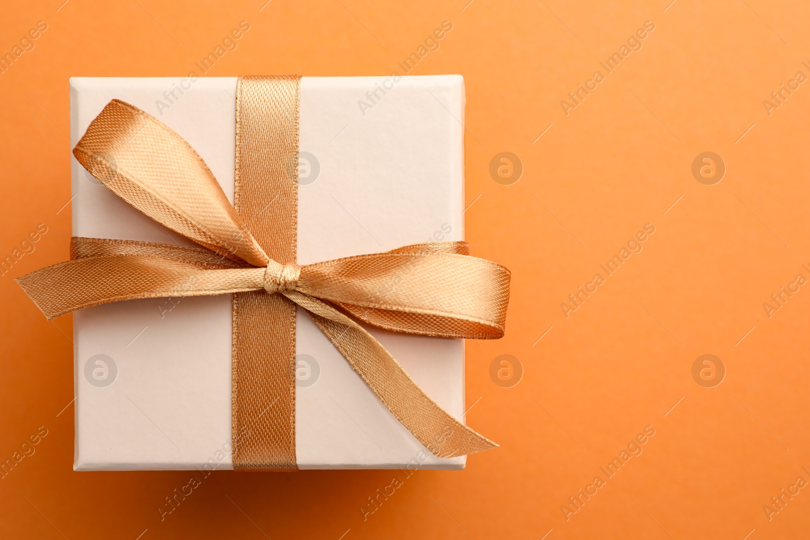 Photo of Beautiful gift box with golden bow on orange background, top view. Space for text