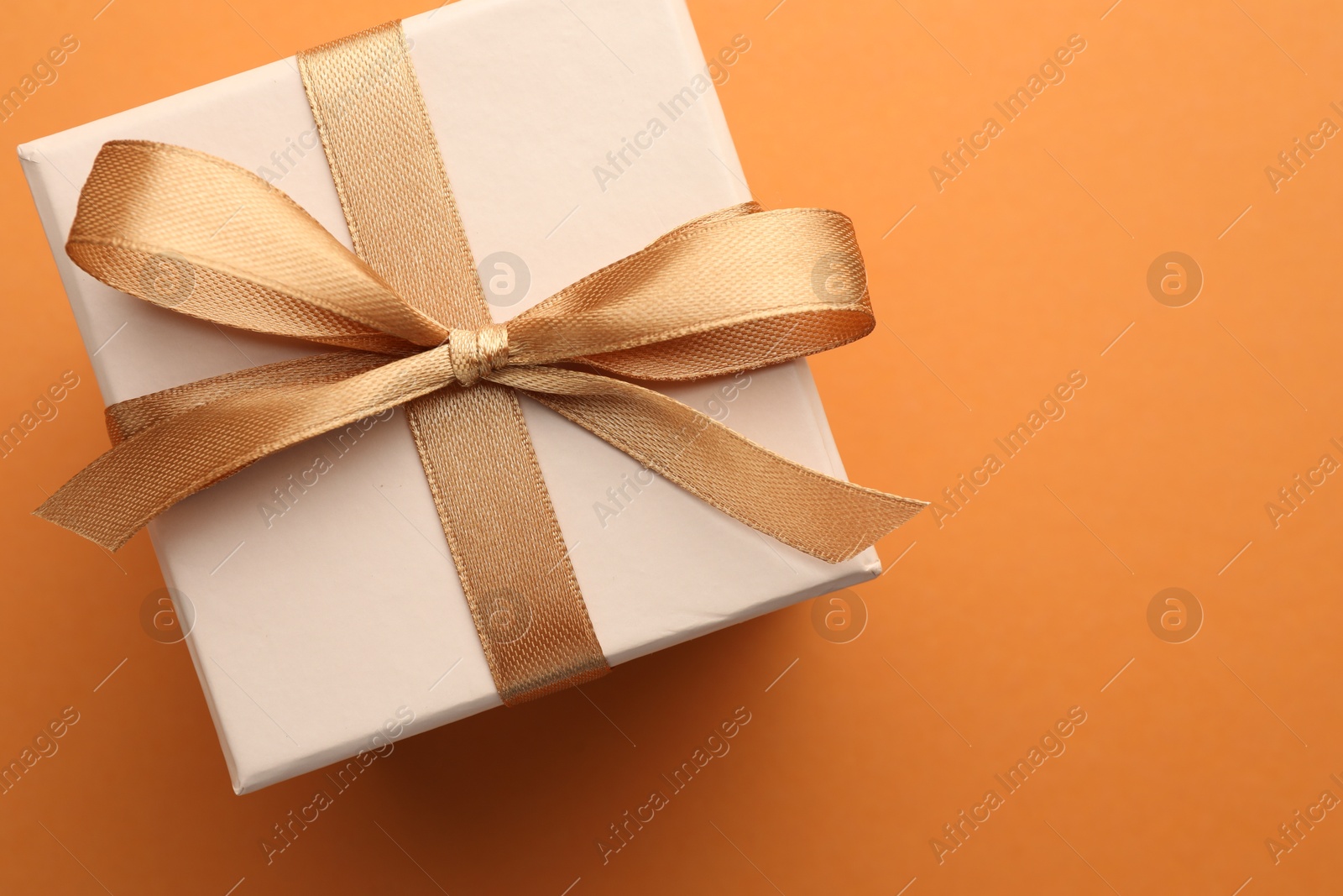 Photo of Beautiful gift box with golden bow on orange background, top view. Space for text