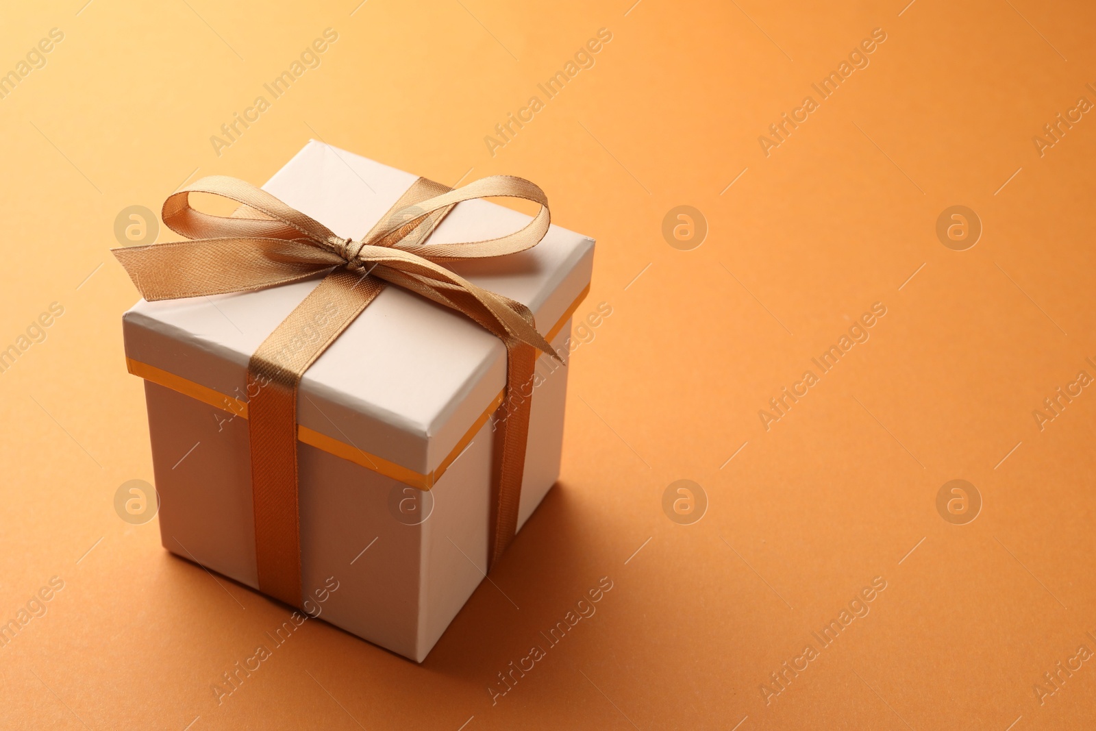 Photo of Beautiful gift box with golden bow on orange background, space for text