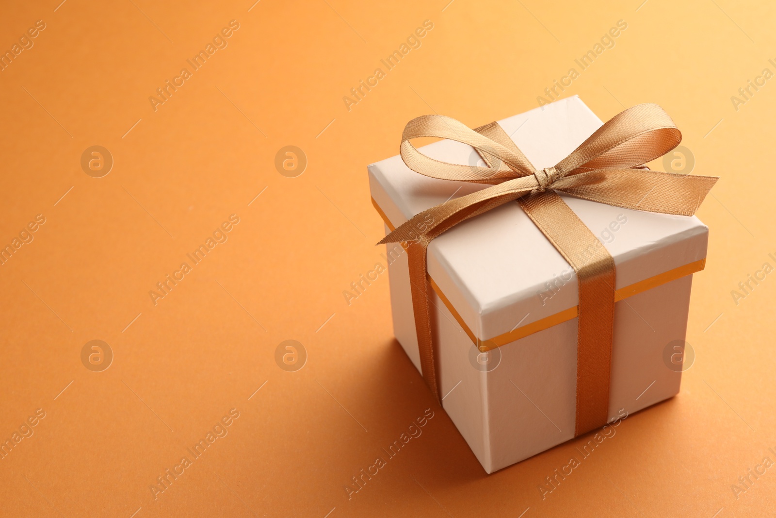 Photo of Beautiful gift box with golden bow on orange background, space for text