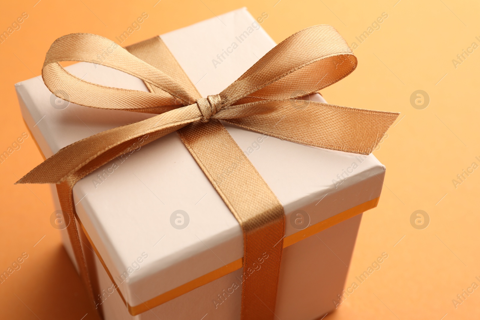 Photo of Beautiful gift box with golden bow on orange background, closeup