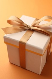 Photo of Beautiful gift box with golden bow on orange background, closeup