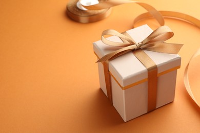 Photo of Beautiful gift box with golden bow and ribbon on orange background, closeup. Space for text