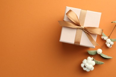 Photo of Beautiful gift box with golden bow and cotton flowers on orange background, top view. Space for text