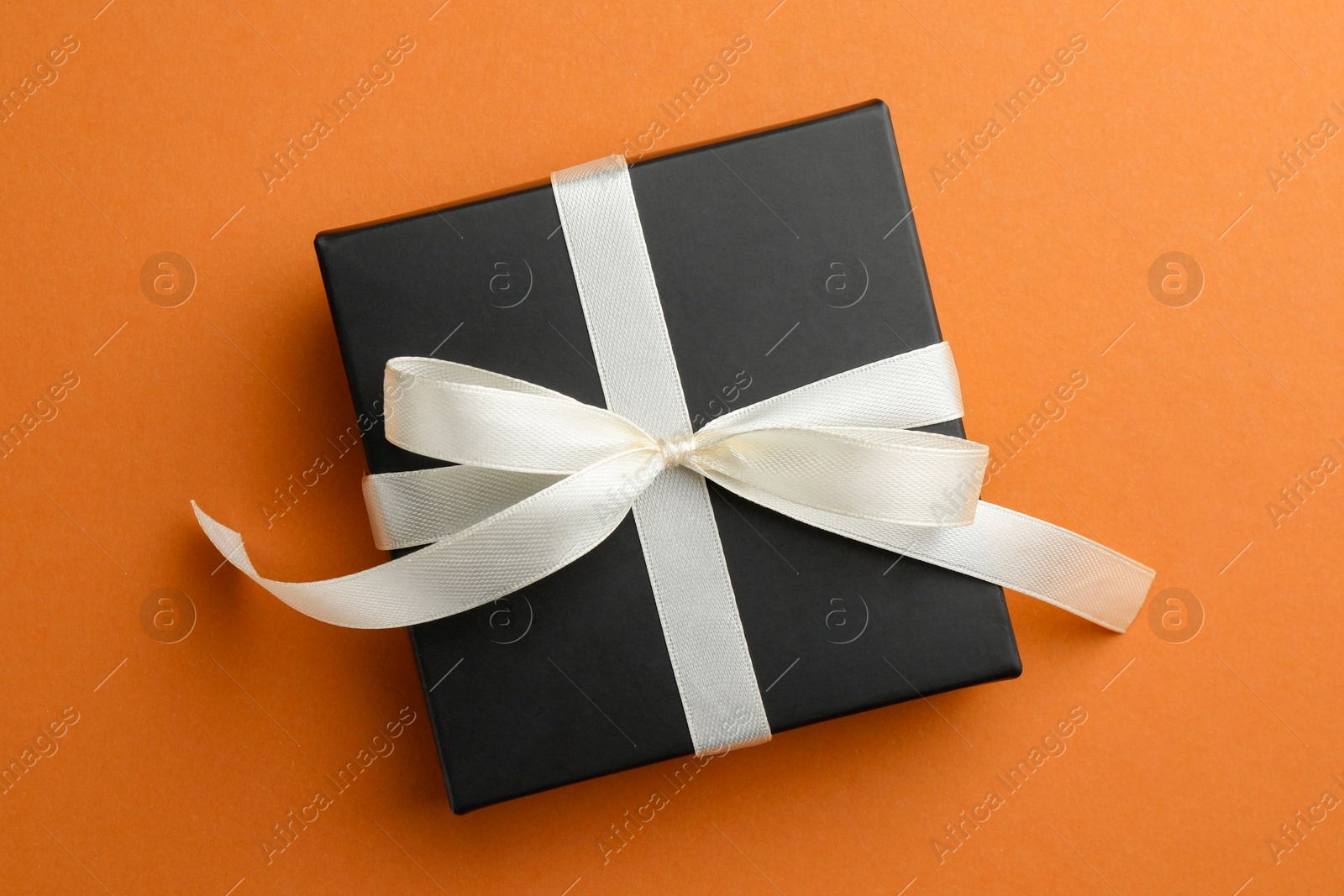 Photo of Beautiful gift box with bow on orange background, top view