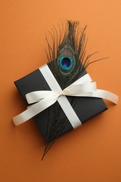 Beautiful gift box and peacock feather on orange background, top view