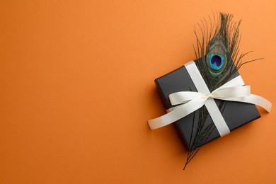 Photo of Beautiful gift box and peacock feather on orange background, top view. Space for text