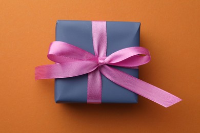 Photo of Beautiful gift box with pink bow on orange background, top view