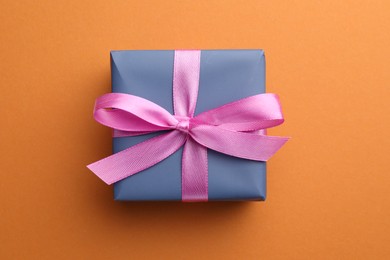 Photo of Beautiful gift box with pink bow on orange background, top view