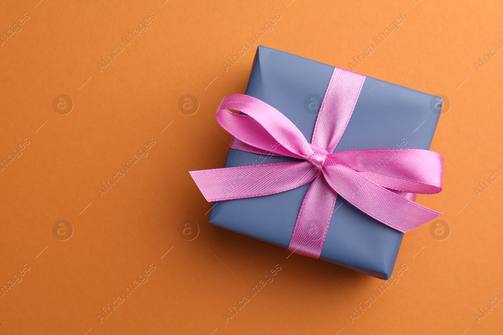 Photo of Beautiful gift box with pink bow on orange background, top view. Space for text