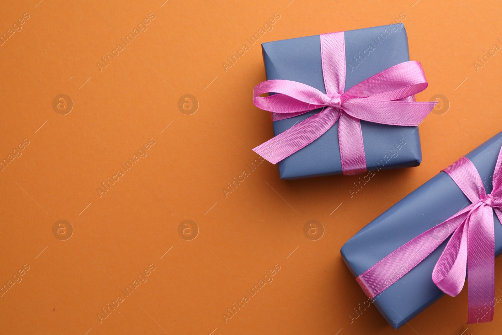 Photo of Beautiful gift boxes with pink bows on orange background, top view. Space for text