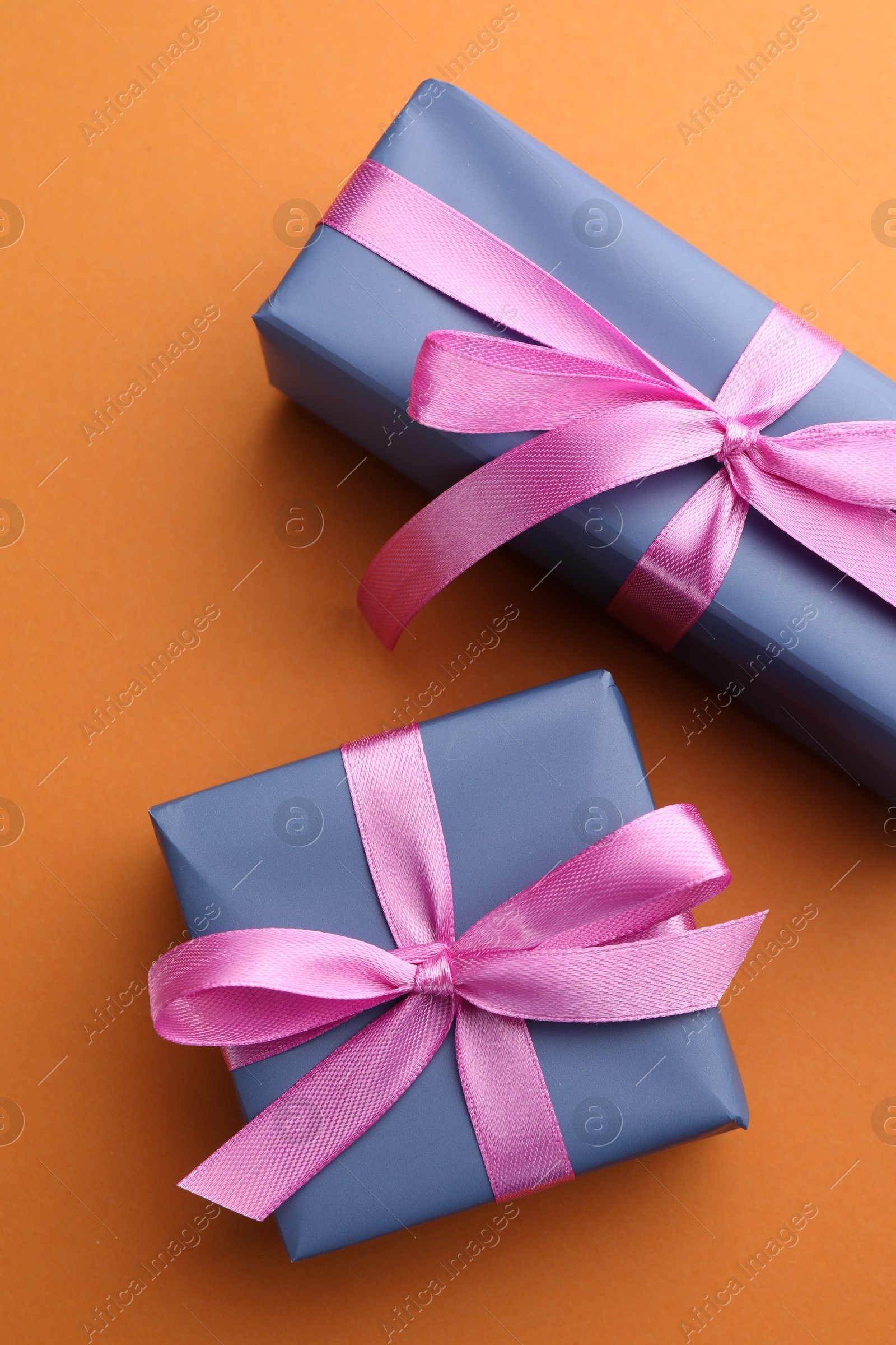 Photo of Beautiful gift boxes with pink bows on orange background, top view