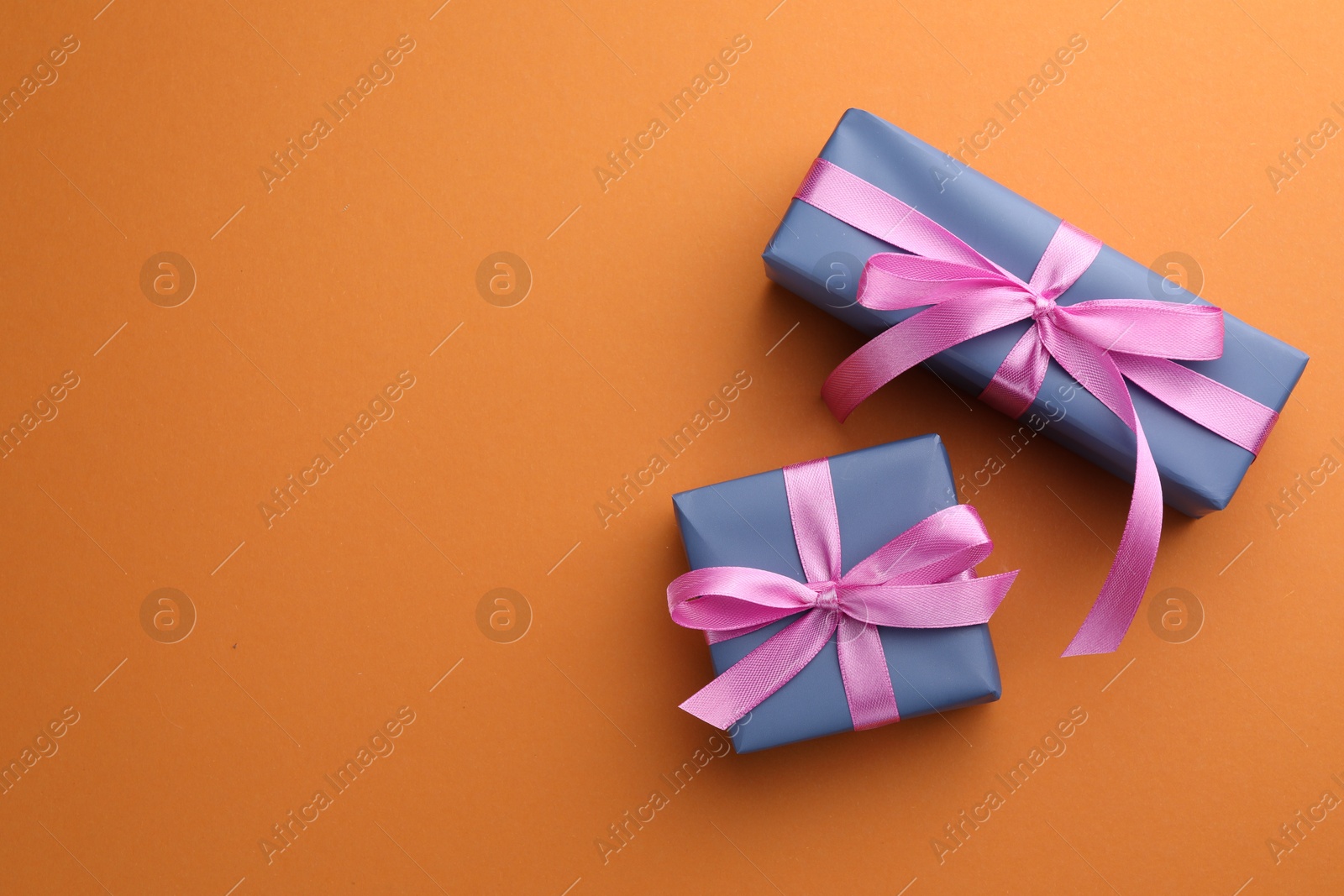 Photo of Beautiful gift boxes with pink bows on orange background, top view. Space for text