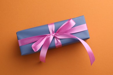 Photo of Beautiful gift box with pink bow on orange background, top view