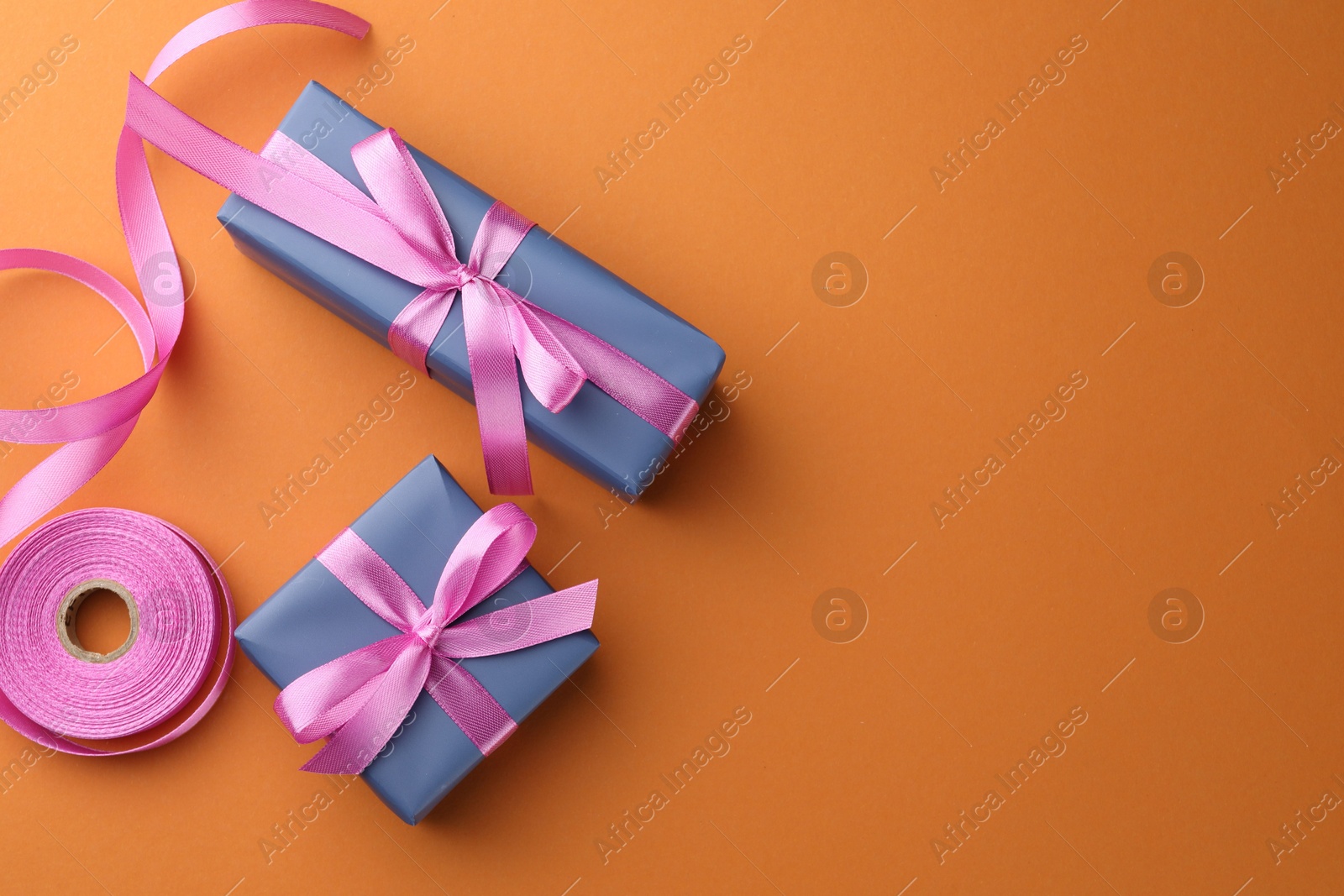 Photo of Beautiful gift boxes with pink bows and ribbon on orange background, top view. Space for text