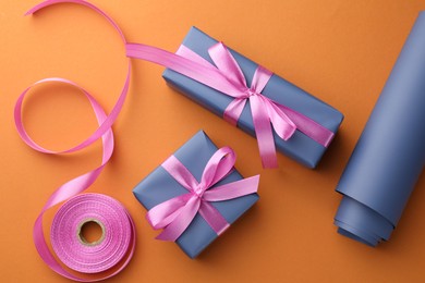 Beautiful gift boxes with pink bows, ribbon and roll of wrapping paper on orange background, flat lay