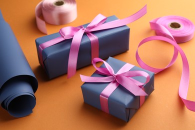 Photo of Beautiful gift boxes with pink bows, ribbons and roll of wrapping paper on orange background