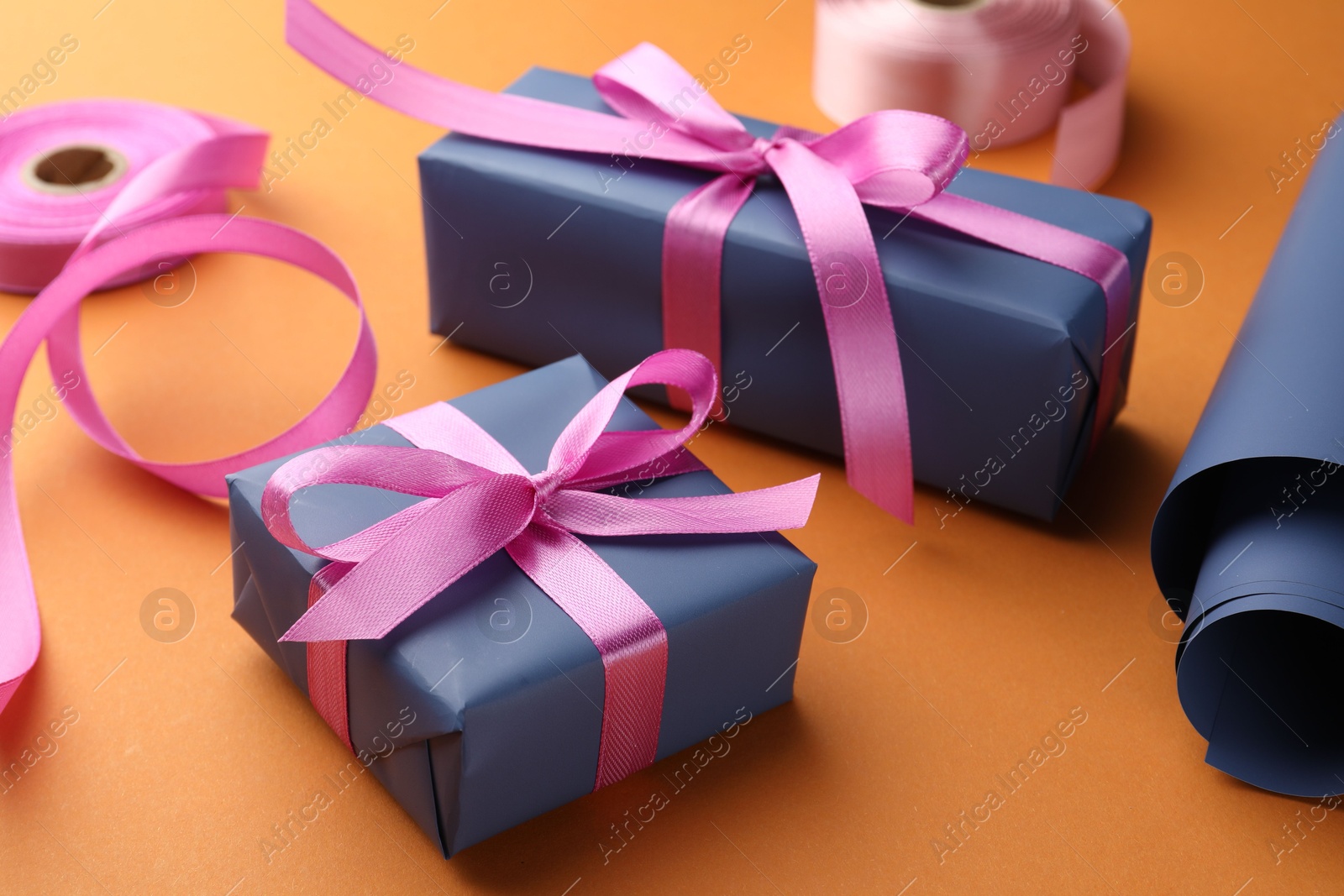 Photo of Beautiful gift boxes with pink bows, ribbons and roll of wrapping paper on orange background