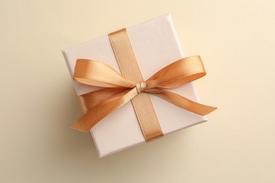 Beautiful gift box with golden bow on beige background, top view