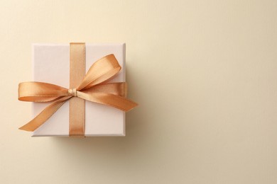 Photo of Beautiful gift box with golden bow on beige background, top view. Space for text