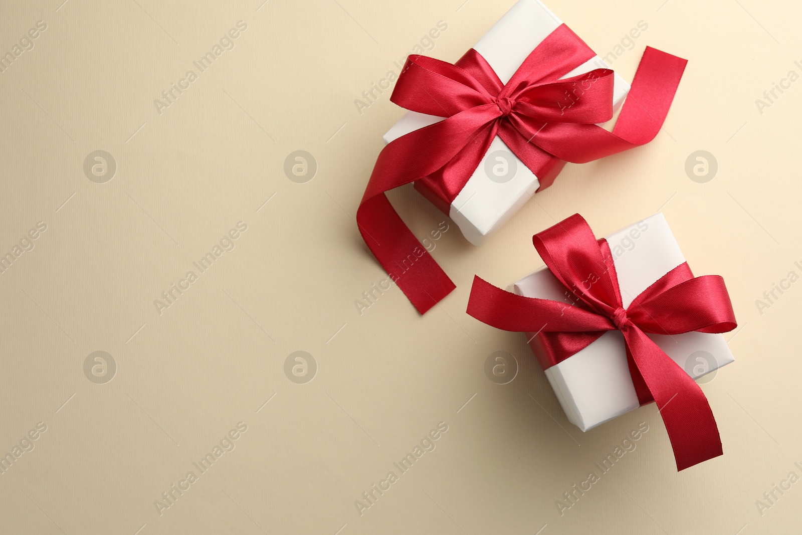 Photo of Beautiful gift boxes with red bows on beige background, top view. Space for text