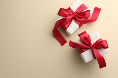 Photo of Beautiful gift boxes with red bows on beige background, top view. Space for text