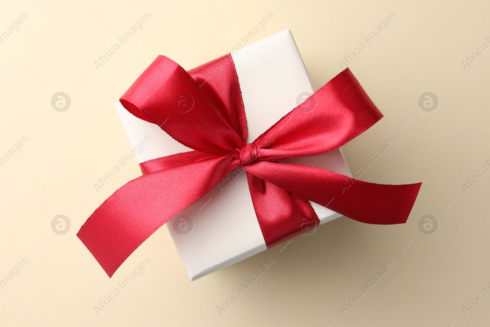 Photo of Beautiful gift box with red bow on beige background, top view