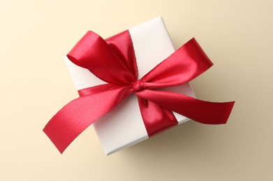 Photo of Beautiful gift box with red bow on beige background, top view